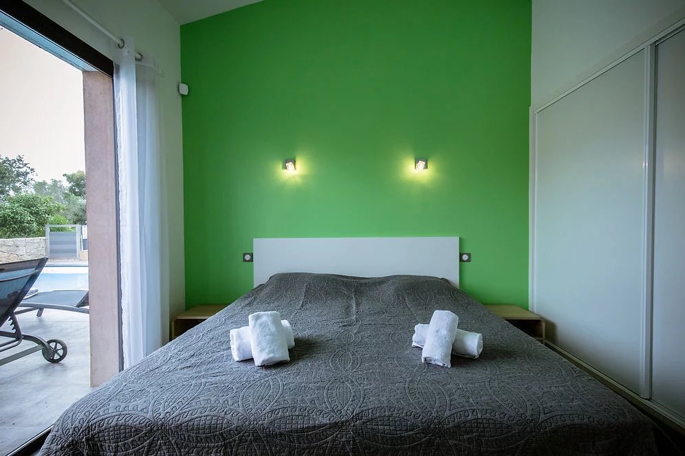 Chambre de villa contemporaine à Porto-Vecchio Chambre d'une villa contemporaine avec mur vert et lit double, serviettes blanches sur le lit.