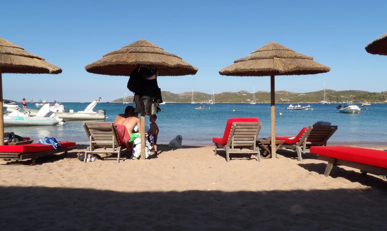 Beach in Bonifacio Beach with parasols and sun loungers, view of the sea and boats in the distance.