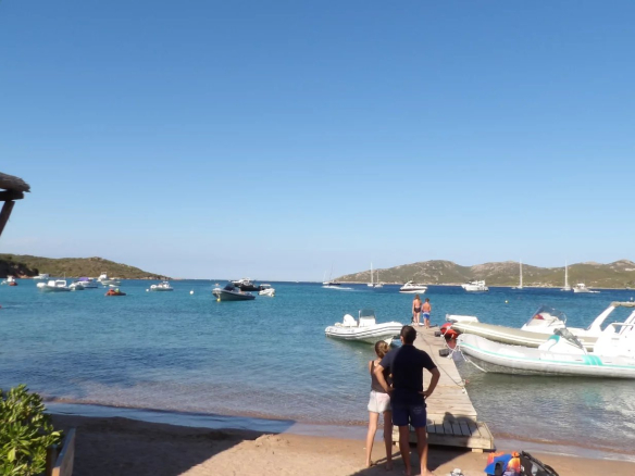 Beach with boats at anchor and people on a pontoon in Bonifacio.