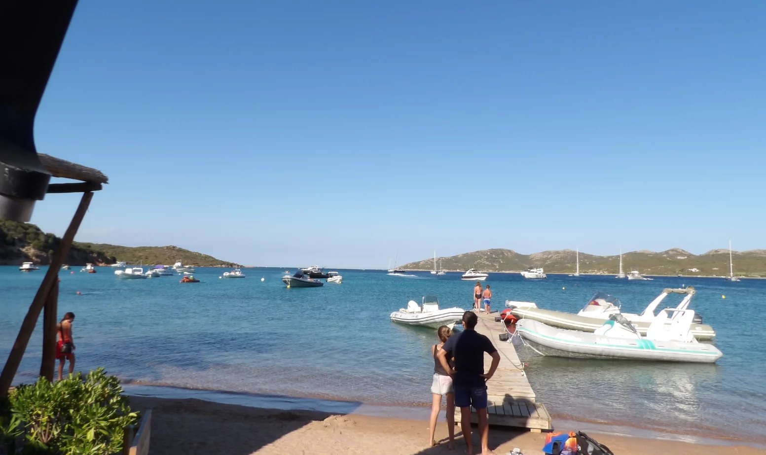 View of the beach in Bonifacio Beach with boats at anchor and people on a pontoon in Bonifacio.