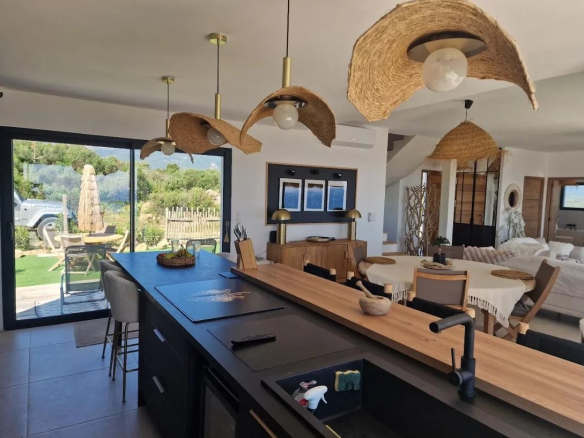Interior of a modern villa with open kitchen and living room, overlooking garden and sea.
