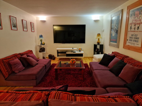 Intérieur d'une villa avec canapés colorés, télévision et décoration murale.