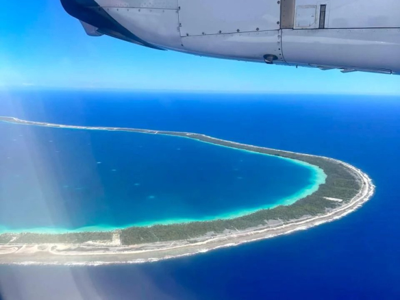 Vue aérienne de l'île de Takapoto avec lagon turquoise et végétation.