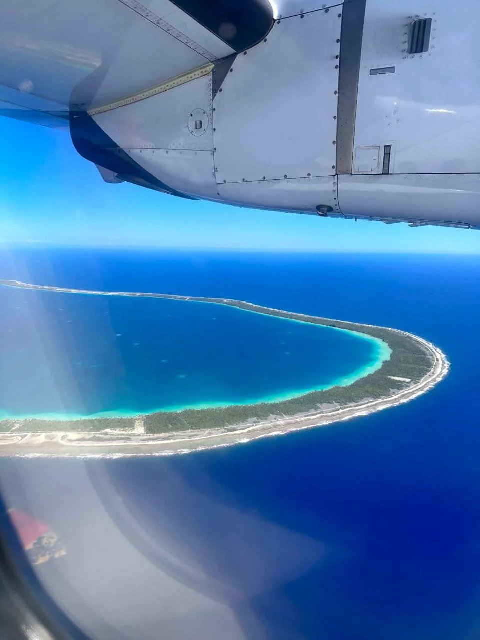 Vue aérienne de l'île de Takapoto avec lagon turquoise et végétation.