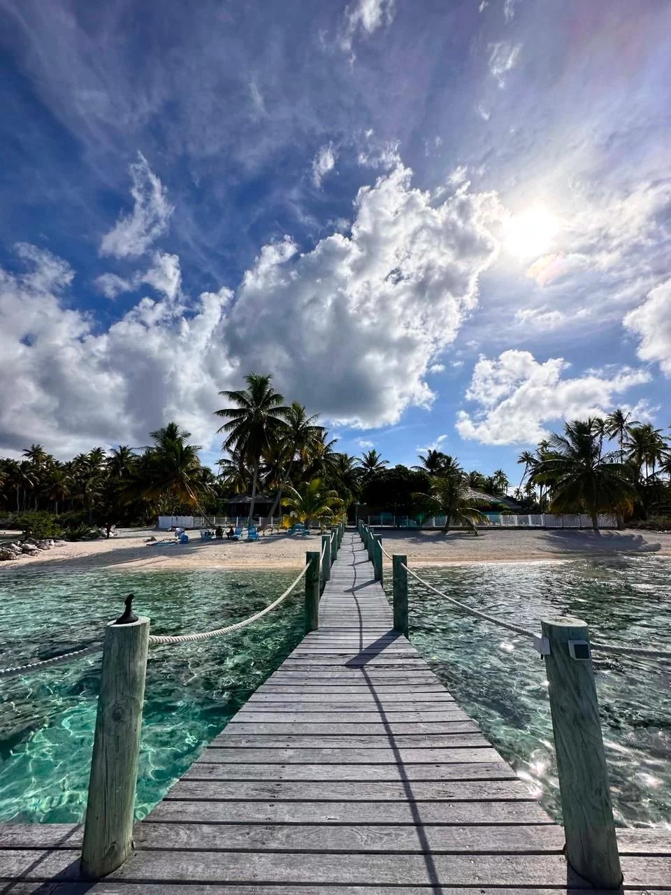 Pont en bois menant à une plage sur l'île de Takapoto, avec des palmiers et une eau turquoise