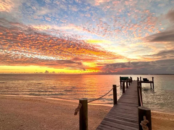 Un ponton en bois sur une plage avec un coucher de soleil sur l'île de Takapoto.