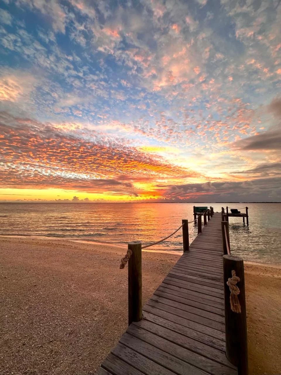Un ponton en bois sur une plage avec un coucher de soleil sur l'île de Takapoto.