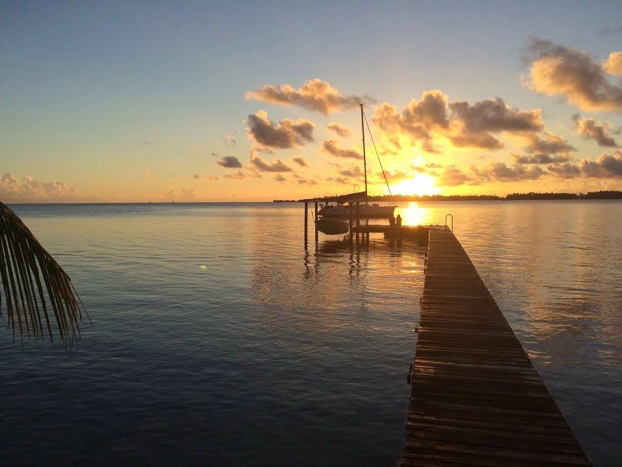 Coucher de soleil sur un ponton à Takapoto, îles Tuamotu, avec un bateau amarré.
