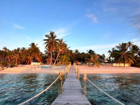 Pont en bois menant à une plage avec des palmiers sur l'île de Takapoto