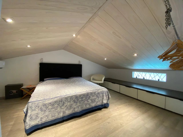 Chambre d'un appartement style loft à Papeete, avec un lit, un banc et un éclairage moderne.