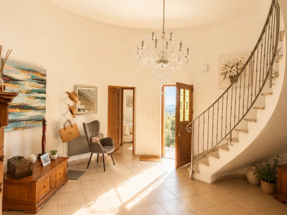 Intérieur d'une demeure avec un escalier en colimaçon et un chandelier, lumière naturelle entrant par les fenêtres.