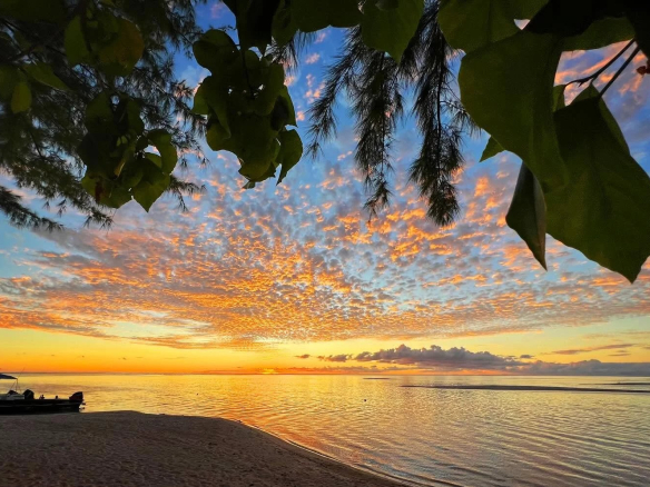 Coucher de soleil sur une plage de Tikehau, Polynésie française, avec des nuages colorés et un reflet sur l'eau.