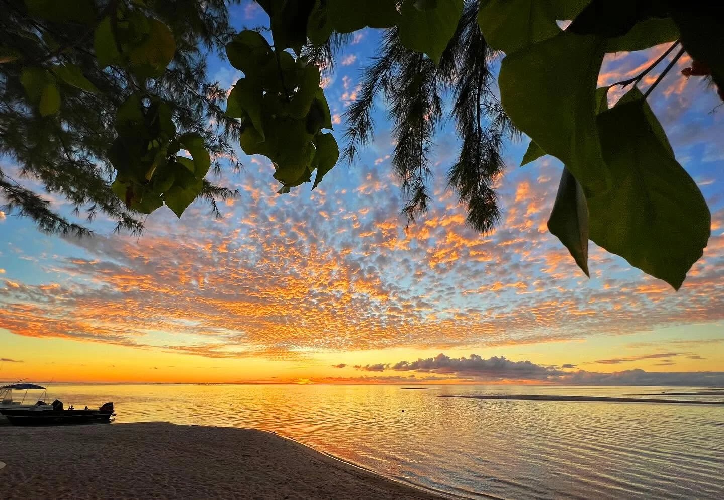 Coucher de soleil à Tikehau Coucher de soleil sur une plage de Tikehau, Polynésie française, avec des nuages colorés et un reflet sur l'eau.
