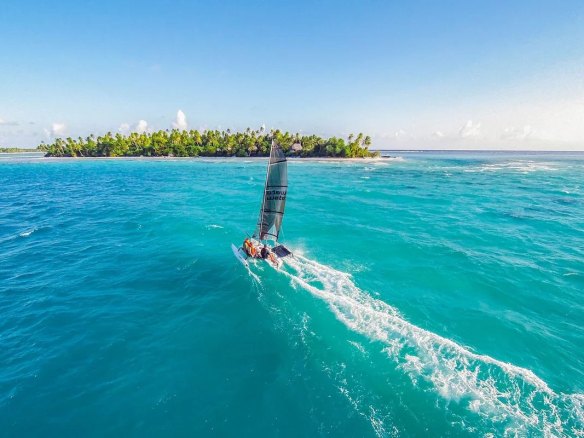 Un catamaran naviguant sur des eaux turquoise près d'une île tropicale à Tikehau, Polynésie française.