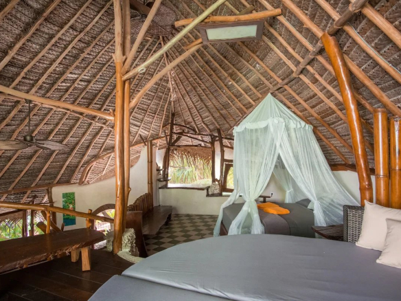 Intérieur d'un éco-lodge de luxe avec un toit en bambou et des lits confortables.