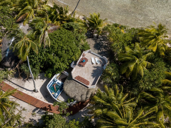 Vue aérienne d'un éco-lodge de luxe avec bungalows en bord de mer entourés de palmiers à Tikehau, Polynésie française.