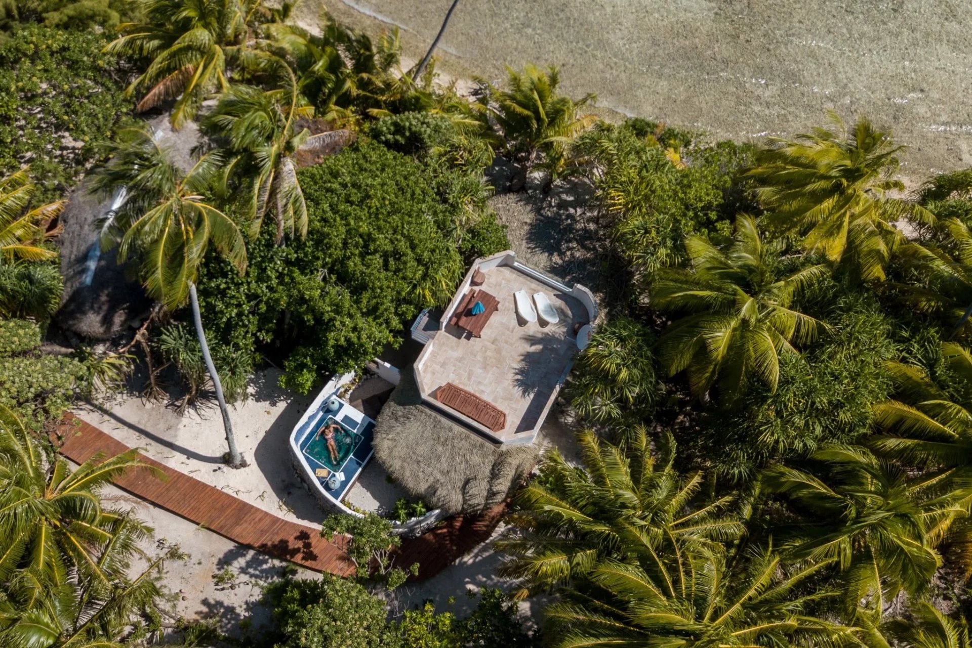 Éco-lodge de luxe à Tikehau Vue aérienne d'un éco-lodge de luxe avec bungalows en bord de mer entourés de palmiers à Tikehau, Polynésie française.