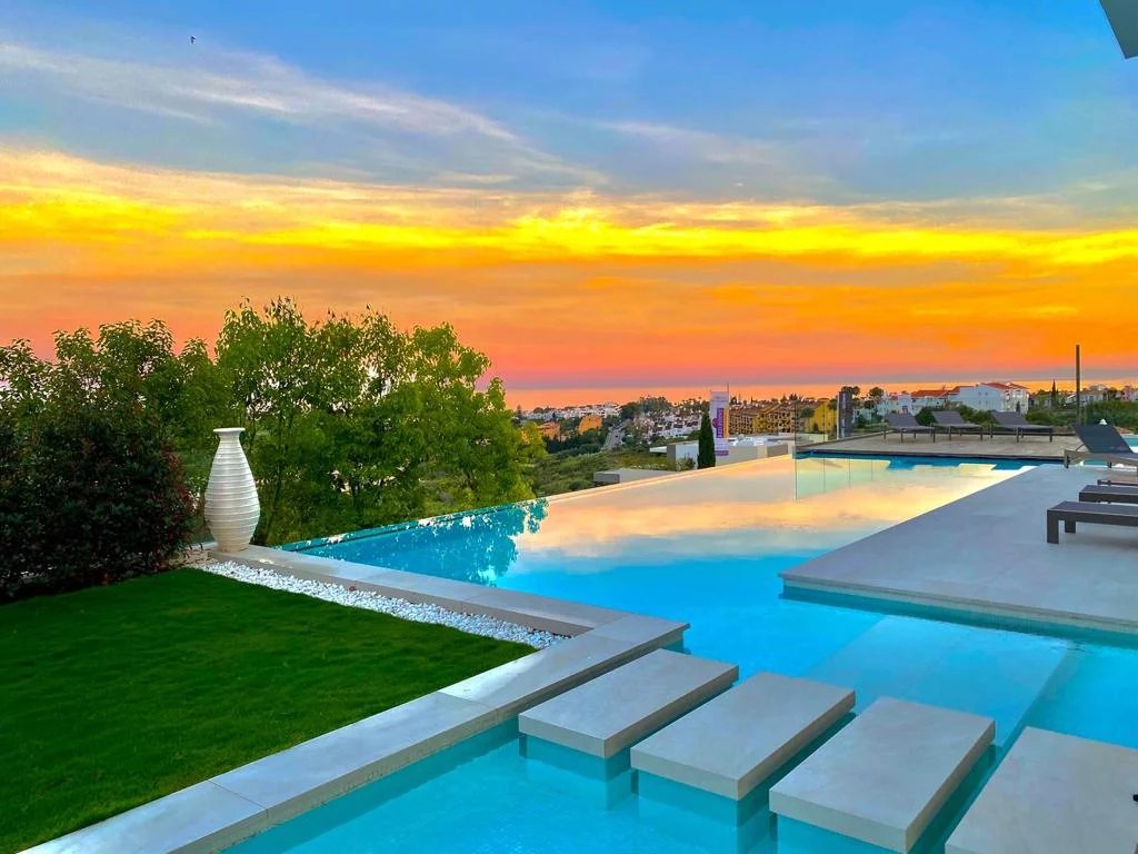 Vue panoramique d'une villa de luxe avec piscine à débordement à Los Flamingos, Marbella, au coucher de soleil.