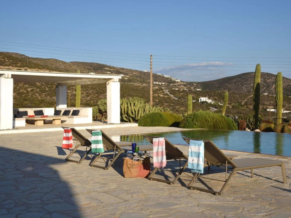 Vue de la piscine et du jardin de la villa à Paros, avec des transats et un espace de détente.