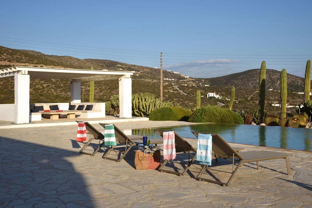 Villa d’exception à Paros Vue de la piscine et du jardin de la villa à Paros, avec des transats et un espace de détente.