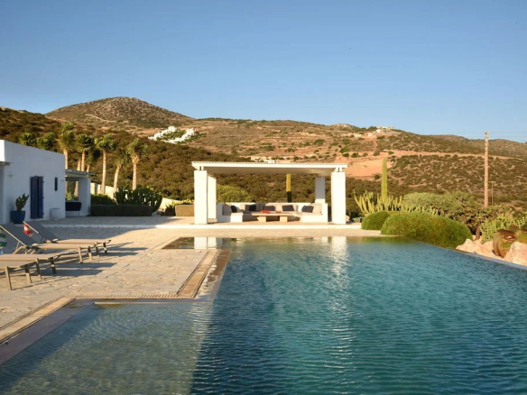 Vue de la piscine et du salon extérieur d'une villa à Farangas, Paros, avec paysage montagneux en arrière-plan.