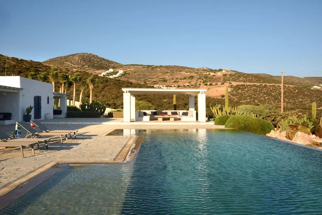 Villa d’exception à Paros Vue de la piscine et du salon extérieur d'une villa à Farangas, Paros, avec paysage montagneux en arrière-plan.