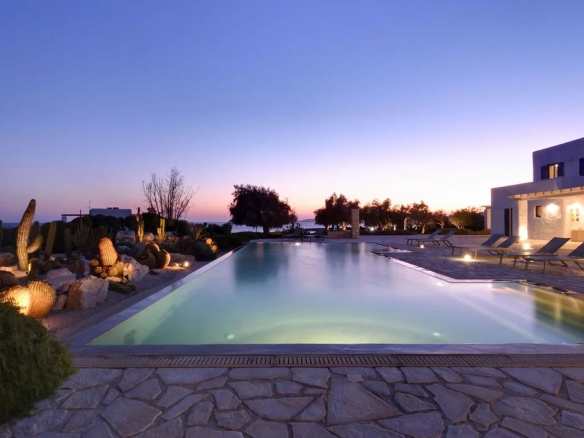 Vue d'une piscine à débordement avec des chaises longues et un paysage de coucher de soleil à Paros.