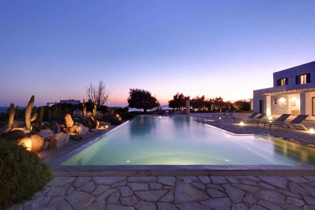 Villa d’exception à Paros Vue d'une piscine à débordement avec des chaises longues et un paysage de coucher de soleil à Paros.