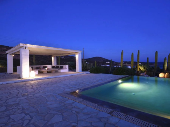 Villa moderne avec piscine et espace de détente à Paros, vue sur la mer Égée au crépuscule.