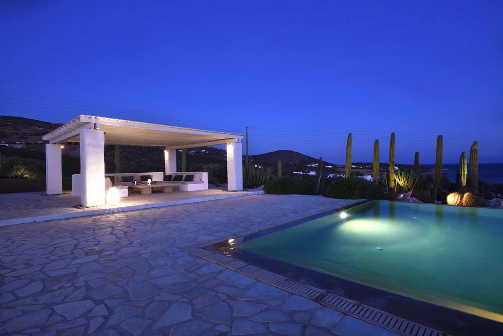 Villa d’exception à Paros Villa moderne avec piscine et espace de détente à Paros, vue sur la mer Égée au crépuscule.