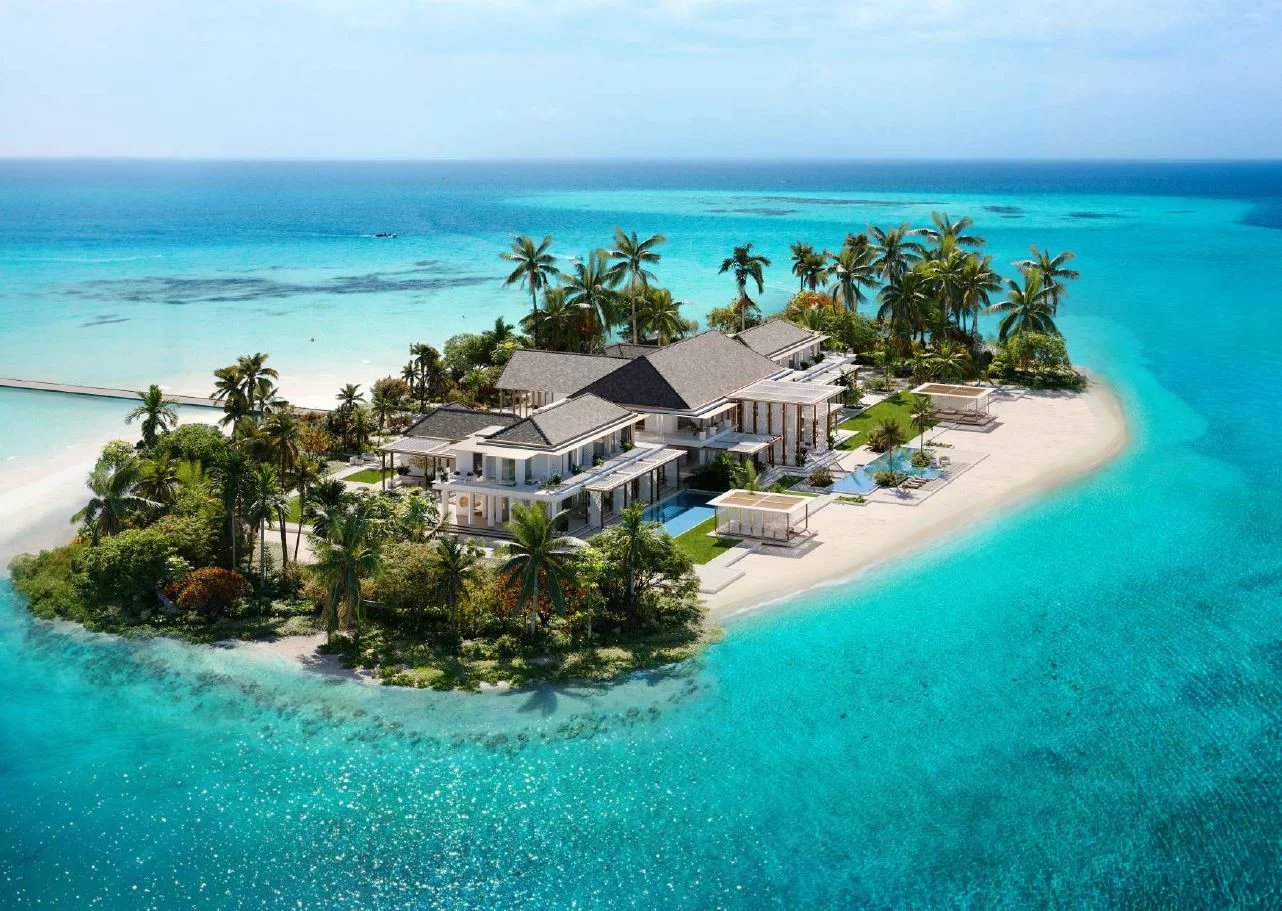 Vue aérienne d'une villa de luxe sur une île aux Maldives, entourée d'eau turquoise et de palmiers.