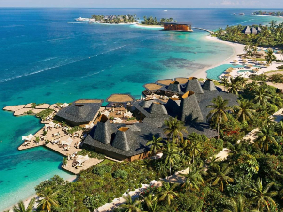 Vue aérienne d'un complexe de villas de luxe aux Maldives, entouré de plages et de palmiers.