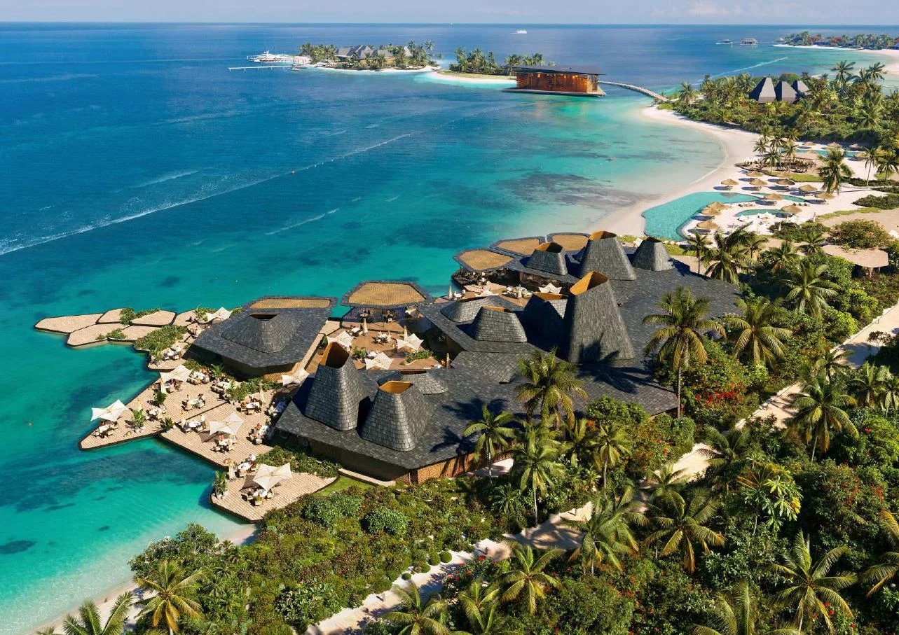 Vue aérienne d'un complexe de villas de luxe aux Maldives, entouré de plages et de palmiers.