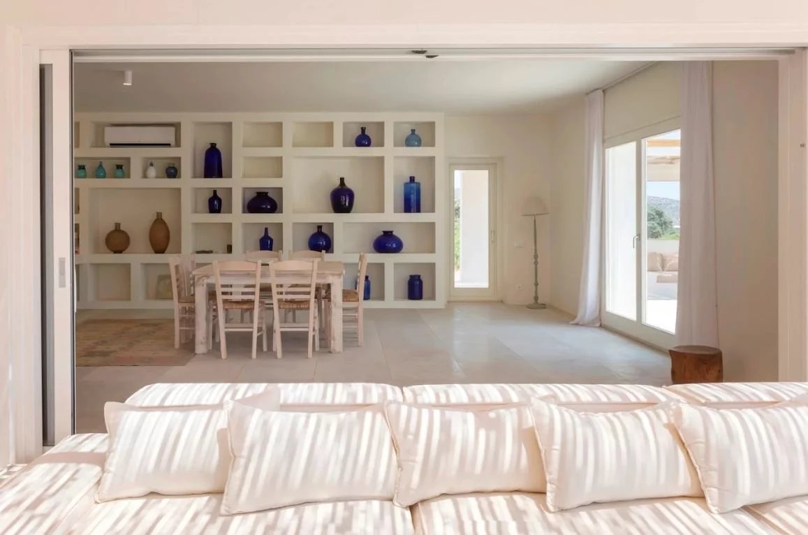 Intérieur d’une villa de luxe à Antiparos Intérieur d'une villa de luxe à Antiparos, avec un salon lumineux et une salle à manger décorée de vases en verre.