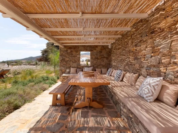 Terrasse en pierre avec mobilier en bois et coussins, entourée de nature à Antipaxos, Grèce.