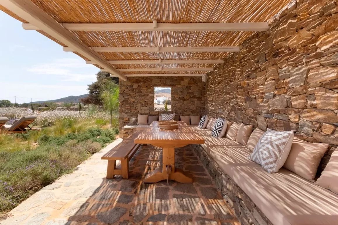 Terrasse de villa à Antipaxos Terrasse en pierre avec mobilier en bois et coussins, entourée de nature à Antipaxos, Grèce.