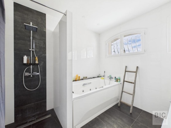 Salle de bain moderne avec douche et baignoire, fenêtres laissant entrer la lumière.