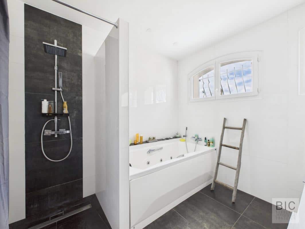 Salle de bain moderne avec douche et baignoire, fenêtres laissant entrer la lumière.