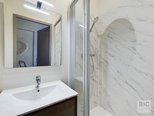 Salle de bain moderne avec douche et miroir, murs en marbre blanc.