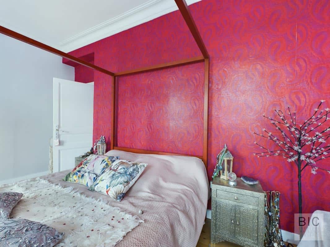 Chambre à coucher élégante Chambre avec un lit à baldaquin et un mur décoré de motifs rouges.