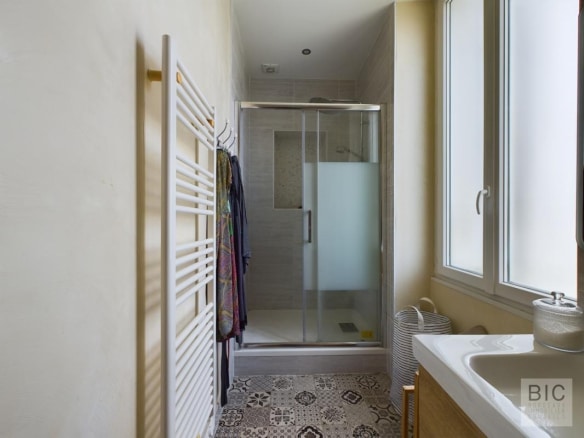 Salle de bain moderne avec douche et lavabo, murs clairs et carrelage décoratif.