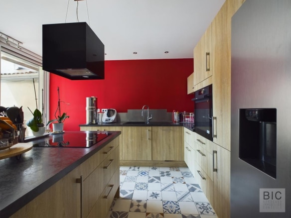 Cuisine moderne avec des meubles en bois et un mur rouge, carrelage décoratif au sol.