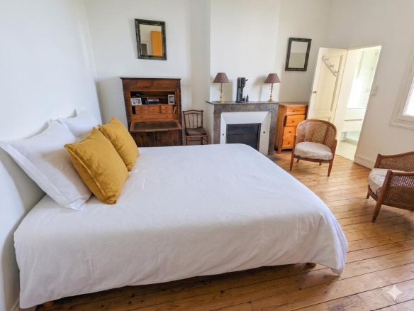 Chambre d'une maison en pierre à Bordeaux, avec lit, fauteuils et cheminée