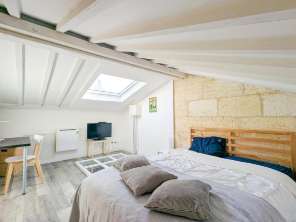 Chambre d'une maison en pierre à Bordeaux avec lit, bureau et fenêtre de toit.