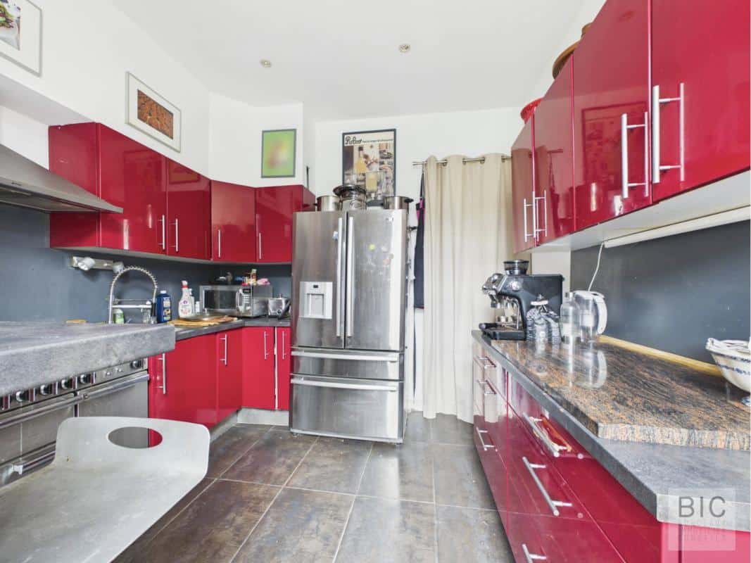 Cuisine d’une maison à Bordeaux Cuisine moderne avec meubles rouges et plan de travail en pierre dans une maison à Bordeaux.
