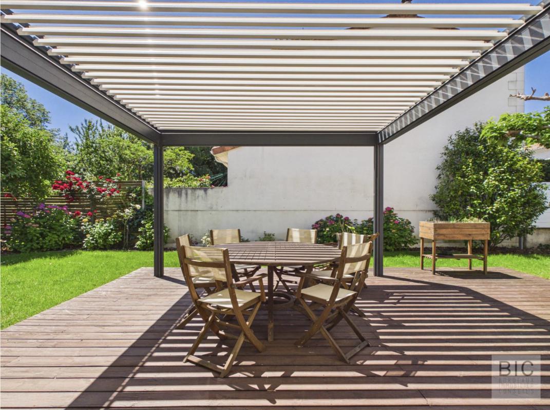 Terrasse de maison à Bordeaux Terrasse en bois avec table et chaises, jardin verdoyant en arrière-plan.