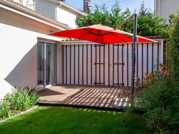Terrasse en bois avec parasol rouge dans un jardin verdoyant.