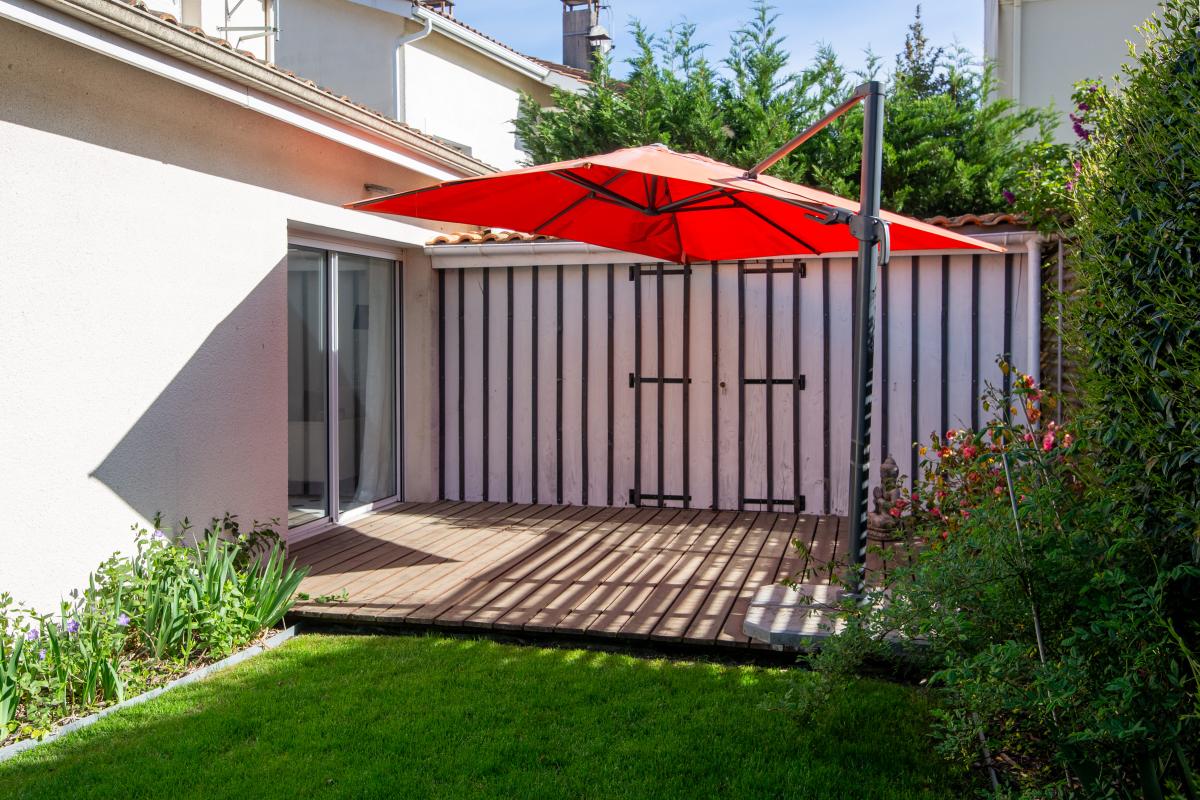 Terrasse de maison à Bordeaux Terrasse en bois avec parasol rouge dans un jardin verdoyant.