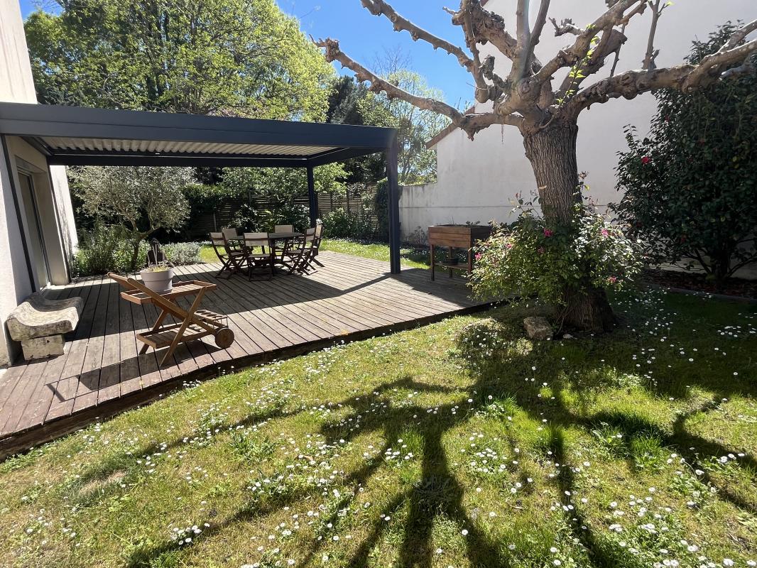 Maison à vendre à Bordeaux Caudéran Terrasse en bois avec mobilier de jardin dans un jardin verdoyant, maison à Bordeaux Caudéran.