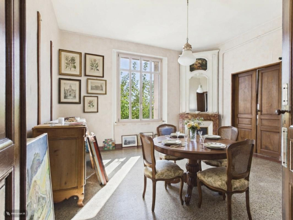 Intérieur d'une maison de maître avec table à manger et fenêtres laissant entrer la lumière.